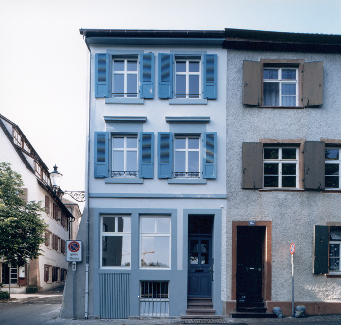 Umbau St. Alban-Rheinweg, Basel-Stadt BS. Das kleine Eckhaus beinhaltet ein überraschend grosses Raumangebot und bietet einen weiten Ausblick auf den Rhein. Das Haus wird erstmals 1486 erwähnt, doch ist für die gegenwärtige Erscheinung vor allem das 19. Jahrhundert prägend. In dieser Zeit wurde es um ein Geschoss aufgestockt und die Fassade wurde neu gestaltet. Der Spezereienladen im Hochparterre ist bis 1970 als solcher geführt worden.  Das Haus ist in seinen Abmessungen sehr schmal und tief. Seine Lage weist jedoch zwei besondere Vorzüge auf: die Nähe zum Rhein mit dem freien Blick auf den Fluss und die südorientierte Dachterrasse auf der Rückseite zum ruhigen Quartier. In Anlehnung an die ehemalige Mischnutzung ist im ehemaligen Laden und im Keller ein Wohnatelier eingerichtet worden. Dieses kann zusammen mit der darüber liegenden Wohnung, welche sich über drei Geschosse erstreckt, vermietet oder auch separat genutzt werden.