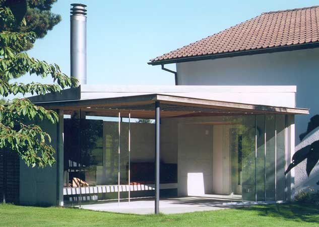 **Gartenpavillon Altnau Thurgau**  Der Gartenpavillon wird als saisonale Erweiterung eines Einfamilienhaus genutzt. Er ist neben den Wohnraum situiert und kann von diesem sowie von der Küche und dem Essraum aus erreicht werden. Die Bodenplatte und die Rückwand sind aus Sichtbeton, das Dach ist einen Holzelementkonstruktion. Grossformatige, rahmenlose Glasscheiben trennen das Innere des Pavillon vom Garten ab, lassen aber den Innenraum mit dem Gartenraum verschmelzen. Das Kanin ragt wegen der guten Zugserscheinung im Feuerraum des Cheminées weit über das dach hinaus.