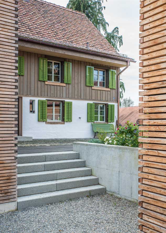 **Die Nordfassade des Taunerhauses Hörhausen mit dem Zugangshof** Dem Altbau mit dem Haupteingang wird duch die Gruppierung des Anbaus und der Garage ein kleiner zugangshof vorgelagert. Diese Hof dient der Ankunft, dem Empfang, aber auch als Spielhof oder Garagenvorplatz. Eine breite Treppe führt an der eche des Neubaus vorbei in den bekiesten Esshof vor dem Essraum im Neubau.