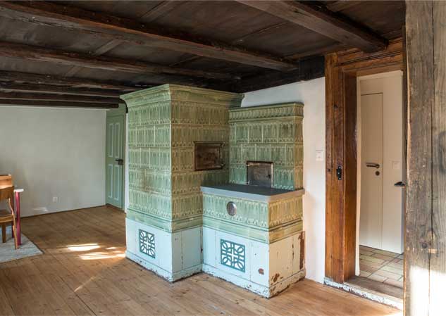 **Wohnzimmer mit Kachelofen im Taunerhaus Hörhausen** Die alte Stube des Kleinbauernhauses oder Taunerhauses in Hörhausen mit dem Kachelofen und den alten Blumentapeten wurde zum Schlafzimmer der Eltern.