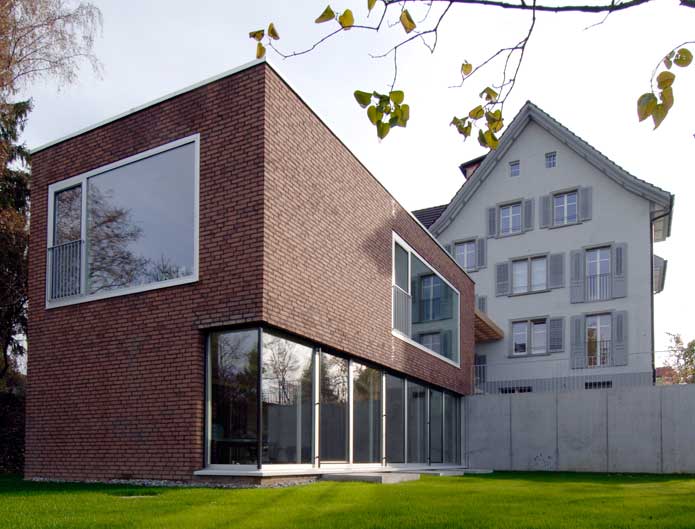 **Wohnheim Im Kanzler, Frauenfeld TG**  Der grosszügige Essraum dient auch als allgemeiner Aufenthaltsraum. Ein breites Fenster mit tiefliegender Brüstung auf Sitzhöhe gibt den Blick nach Westen über das Thurtal und die Stadt Frauenfeld frei. Die nachmittags- und Abendsonne erhell den Raum. In der Verlängerung des Essraumes schliesst sich der Wohnraum an.  Ess- und Wohnraum werden durch einen olivgrünen Raumteiler, ein Schrank für Geschirr und Besteck, unterteilt. Die fenster beider Räume sind aussen bündig angeschlagen sodass sich einen tiefe Fensternische zum darin Sitzen, Liegen oder Wohnschmuck und Nippes aufzustellen ergiebt.