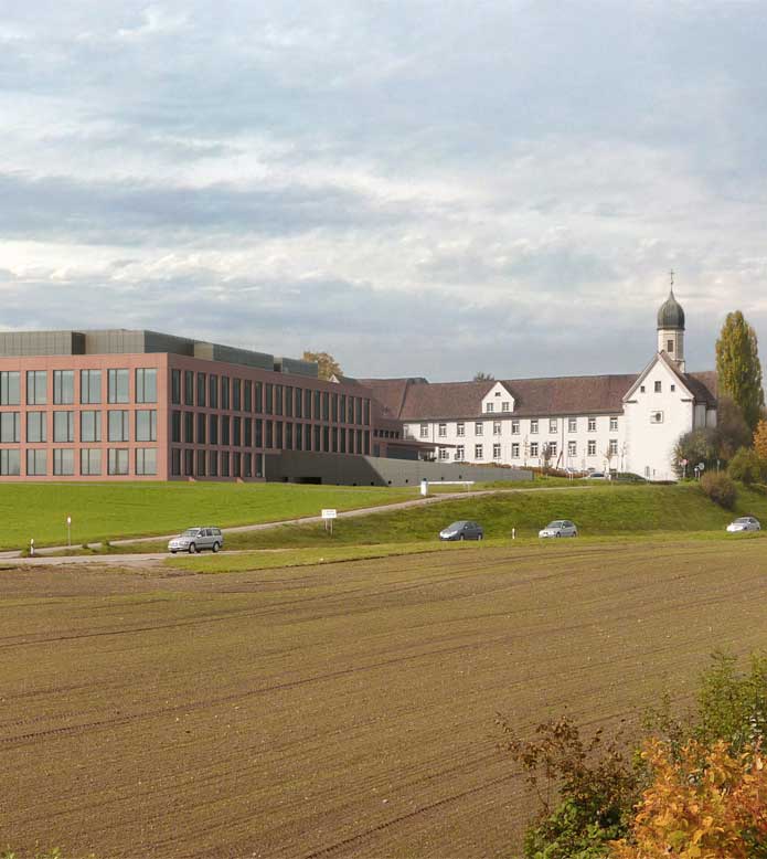 **Neubau Spital Münsterlingen, Münsterlingen TG** Das alte Kloster und die Kloster-Kirche sind als markante Bauten von Weitem erkennbar. Die Erweiterung tritt deshalb leicht von der Hangkante und der Hauptstrasse zurück, so dass der Blick auf den historischen Bestand frei bleibt. In der Höhenentwicklung übernimmt sie die Dachkante der jüngeren, deutlich tieferen Spitaltrakte auf. Die Fassaden der Erweiterung entwickeln sich aus denjenigen der kürzlich sanierten Bettenhäuser und lassen die verschiedenen Gebäudeteile zu einem einheitlichen Erscheinungsbild zusammen wachsen. Im Erdgeschoss befinden sich die Ambulatorien und im Obergeschoss die Operationssäle. Die bestehenden inneren Erschliessungsachsen werden weiter geführt, wobei zwei grosszügige Atrien das Gebäudeinnere belichten und die Orientierung erleichtern.